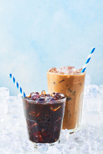 Summer Drink Iced Coffee In A Glass And Ice Coffee With Cream In A Tall Glass Surrounded By Ice On White Marble Table Over Blue Background. Selective Focus, Copy Space For Text.
