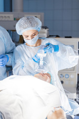 Canvas Print - Pre oxygenation for general anesthesia. Focused surgeon team operating in an operating theatre, blue filter