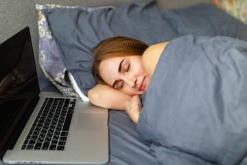 A young blonde is sleeping next to her laptop. The freelancer girl fell asleep from work, completing the project on time on the laptop at night.