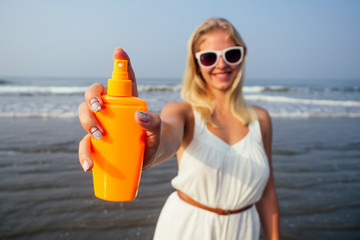 Tan woman applying sun protection lotion in white dress and glasses on the beach