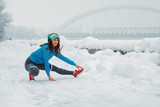 Fototapeta Panele - Young woman stretching legs on snowy day in the city