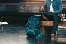 Backpacker Man Sitting On Bench Waiting At Train Station.