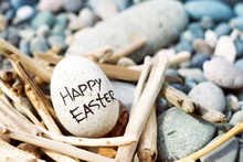 Easter Egg From A Stone With The Inscription Happy Easter In A Decorative Nest From Brushwood On The Sea Pebble Beach.