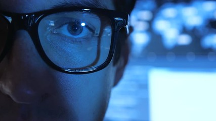 Close up Portrait of IT professional programmer in glasses in cyber security center filled with display screens.