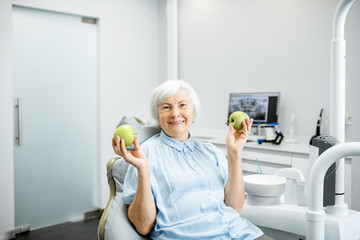 Portrait of a beautiful senior woman with healthy smile holding green apple at the dental office