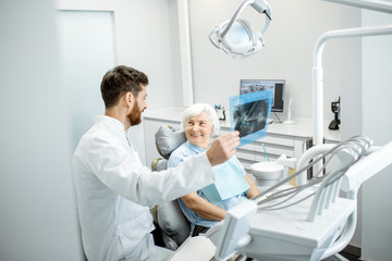 Wall Mural - Happy elder woman during the consultation with handsome dentist showing panoramic x-ray in the dental office