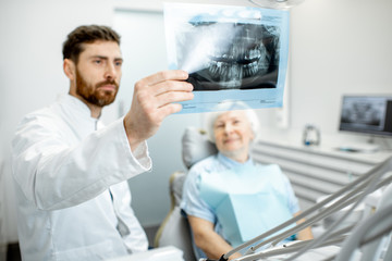 Wall Mural - Happy elder woman during the consultation with handsome dentist showing panoramic x-ray in the dental office