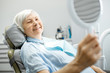 © rh2010 - Happy elderly woman enjoying her beautiful toothy smile looking to the mirror in the dental office