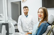 Portrait of a young smiling woman with healthy smile sitting in the dental office with male dentist on the background