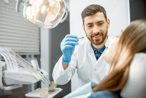 Fototapeta na szkło Handsome dentist making dental examination to a young woman patient in the dental office