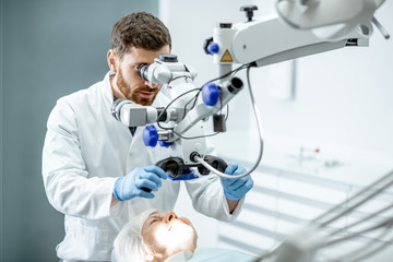 Wall Mural - Male dentist examining senior woman looking on the teeth with professional microscope in the surgery dental office