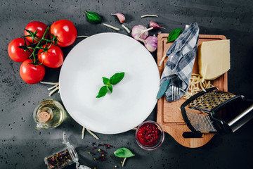 Wall Mural - Top view of an empty white plate with a basil leaf. On the table are arranged various food ingredients such as tomatoes, oil, cheese. Cover the table for food.