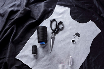Sewing children's handmade t-shirts. Gray fabric and thread on a dark background. Process of tailoring: gray fabric, scissors, thread, tassel and black paint. T-shirt blank
