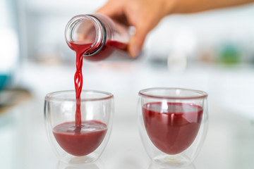 Juice bottle beet drink smoothie woman pouring drinks in cups at home kitchen. Closeup of two glasses with red vegetable juicing cold pressed beverage.