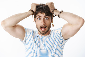 Worried and panicking young confused guy with blue eyes pulling hair out of head and open mouth feeling anxious and scared as realising girlfriend got pregnant being scared of responsibilities