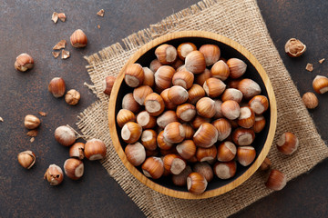 Hazelnuts in a wooden bowl on brown textured background, copy space