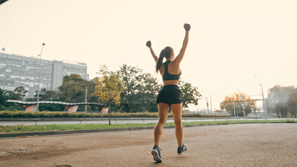 Wall Mural - Backshot of Strong Fitness Girl in Black Athletic Top and Shorts Jogging on Street. She is Celebrating the End of Her Workout with Raised Hands. Athlete is Running in an Urban Environment Under Bridge