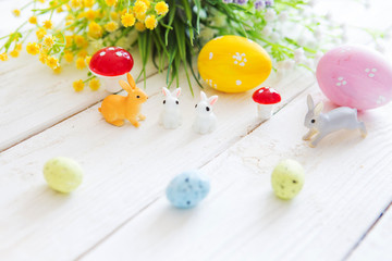 Colorful easter eggs with rabbits or hare toys and flowers on wooden table