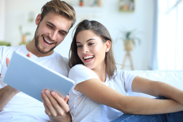 Young couple watching media content online in a tablet sitting on a sofa in the living room.