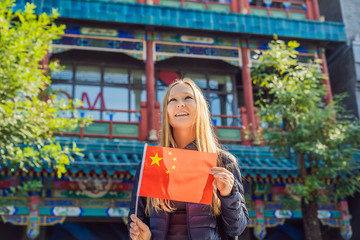Wall Mural - Enjoying vacation in China. Young woman with national chinese flag on the background of the old Chinese street. Travel to China concept. Visa free transit 72 hours, 144 hours in China