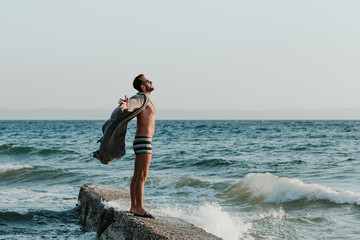 Wall Mural - Young man in a bathrobe on the beach in sunset