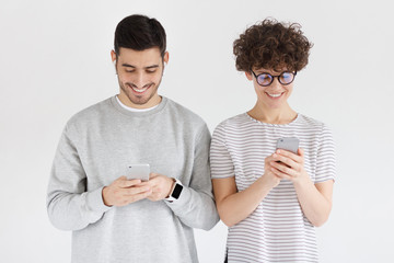 Young happy couple holding smartphones and standing shoulder to shoulder isolated on gray background