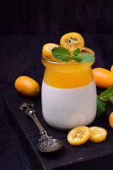 Wall Mural - Creamy panna cotta and orange jelly in a glass jar topped with kumquats and mint against the dark background, Two layered dessert