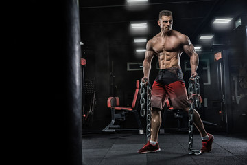 Wall Mural - Young handsome male athlete bodybuilder does exercises for leg muscles, uses chains. Beautiful dark background. Concept - gym sports nutrition diet styroyd health simulators strength power crossfit.