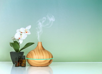 electric essential oils aroma diffuser, oil bottles and flowers on green blue gradient surface with 