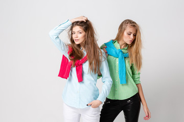 happy girlfriends women in shirts and a sweater on his shoulders. Fashion spring image of two sisters. Colorful colors clothes. Models with Blonde and light brown hair. Looking at camera and smiling.