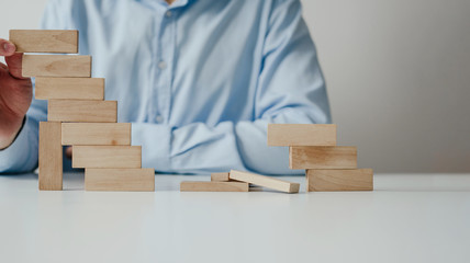 Wall Mural - Businessman in a blue shirt arranges wooden jigsaw blocks. The man arranges empty blocks one on top of the other. Different concepts to supplement with content. Business concept, HR.