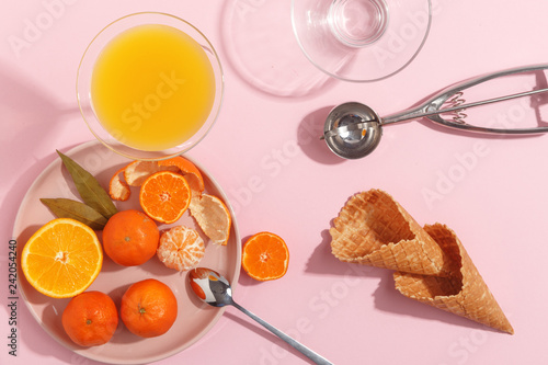 Fotografía Tangerines, waffle cones and ice cream spoon on a pink background