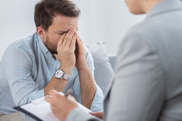 Wall Mural - Handsome sad young businessman with problems during session with counselor