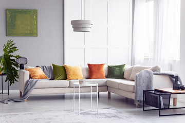 Lamp above table next to corner sofa with pillows in apartment interior with poster. Real photo