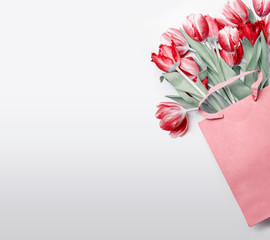 Wall Mural - Red tulips in paper shopping bag on  light gray background. Festive spring flowers bunch. Floral gift composing. Springtime holiday , greeting or sale concept. Copy space for your design