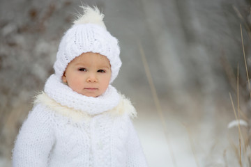 Cute little toddler boy and his older brothers, playing outdoors with snow on a winter day