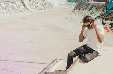 Wall Mural - Young bearded handsome man sitting next to a colorful wall background wearing headphones and empty white t-shirt and sunglasses. Horizontal mock up style