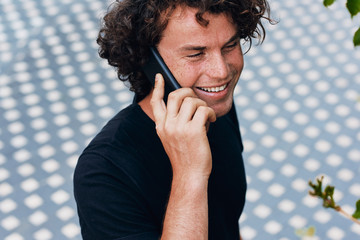 Outdoors image of happy smiling young man standing outdoors talking on the mobile phone. Handsome male making a phone call to his girlfriend. People and lifestyle concept.