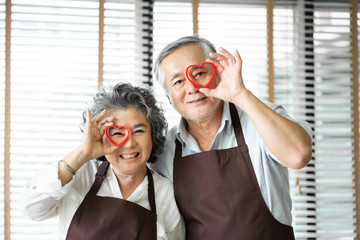 Asian senior couple  holding red cookies cutters over their eyes.