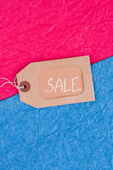 Brown tag with inscription sale on colored background. Cardboard label with inscription sale on blue and pink background. Holiday sales concept.