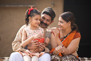 Wall Mural - Indian family holding piggy bank at home