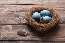 Three Marble Blue Easter Eggs, In A Nest With Feathers On A Wooden Background. The Symbol Of Easter. Copy Space