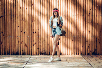 Wall Mural - Stylish young woman standing near wooden background looking at camera and smiling. Hipster ,trendy, lifestyle concept.