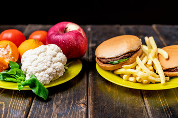 junk food or healthy vegetables and fruits on dark wooden table isolated b