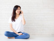 © N_studio - Beautiful of portrait young asian woman talk smart phone and smile sitting on cement concrete brick background, freelance female calling telephone, communication of mobile concept.
