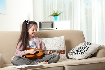 Canvas Print - Cute little girl playing guitar on sofa in room. Space for text