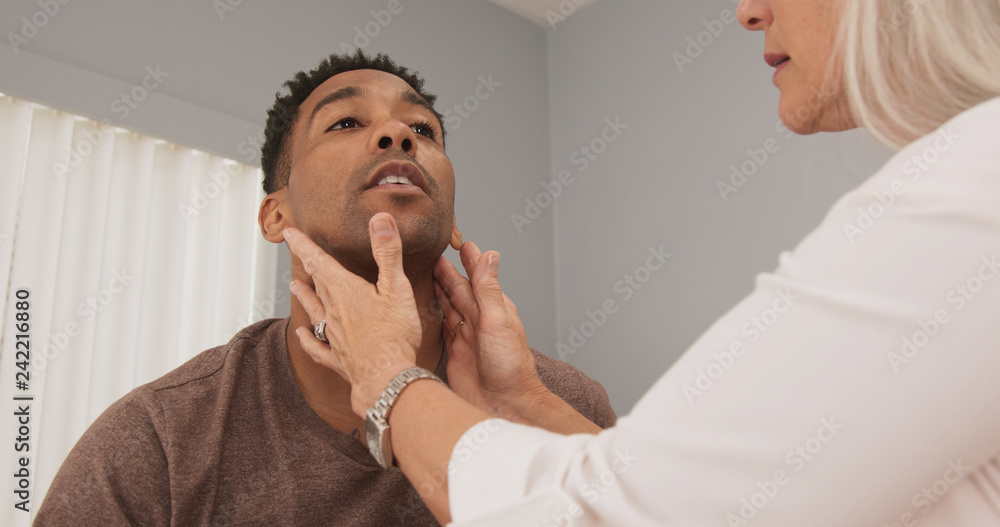 Mature female doctor checking male patients neck for swollen thyroid or lymph nodes. Senior doctor examining patients neck indoors medical clinic  - obrazy, fototapety, plakaty 