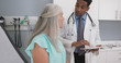 © Mark Adams - Male millennial MD taking notes on electronic tablet while listening to senior female patient. Elderly woman explaining health condition to young doctor while he uses computer pad