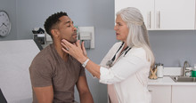 Portrait Of Senior Medical Doctor Examining Patients Neck For Swollen Thyroid. Attractive Black Male Having Doctor Checkup At Health Clinic
