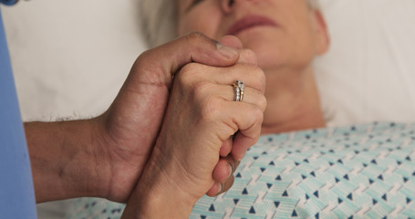 Wall Mural - Close up of african-american nurses hand holding caucasian patients hand in hospital. Portrait of ill elderly woman lying in bed holding hands with registered nurse